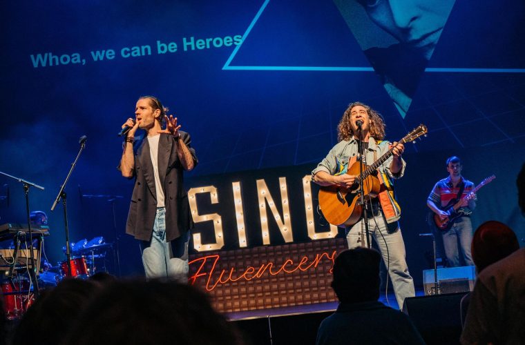 Een volle zaal in Phil Haarlem zingt samen Bowie-nummers onder leiding van Maarten en Tijmen, met 'Heroes' als thema.